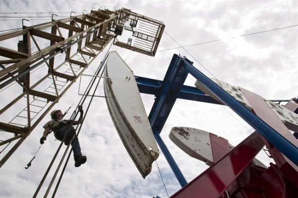 In this July 26, 2011 photo, a worker hangs from an oil derrick outside of …